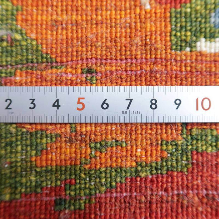 手織りのギャッベラグの織り目が定規で計測され、ウールの質感と鮮やかな色合いが際立っている。