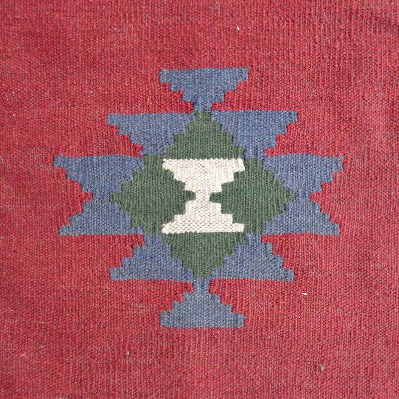 赤い背景に幾何学模様が丁寧に織られたギャッベのラグがあり、ペルシャ絨毯専門店の通販で手に入るウールの質感が際立っている。