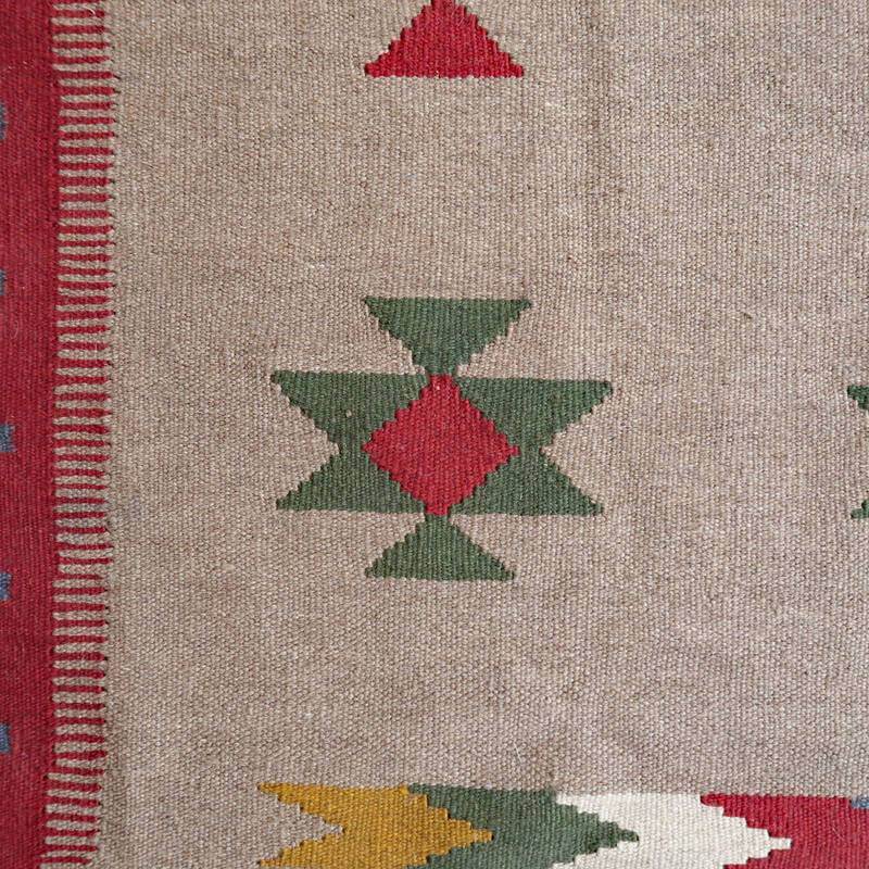 緻密に手織りされたウールのペルシャ絨毯は、赤と緑の幾何学模様が落ち着いたベージュの背景に映えている。