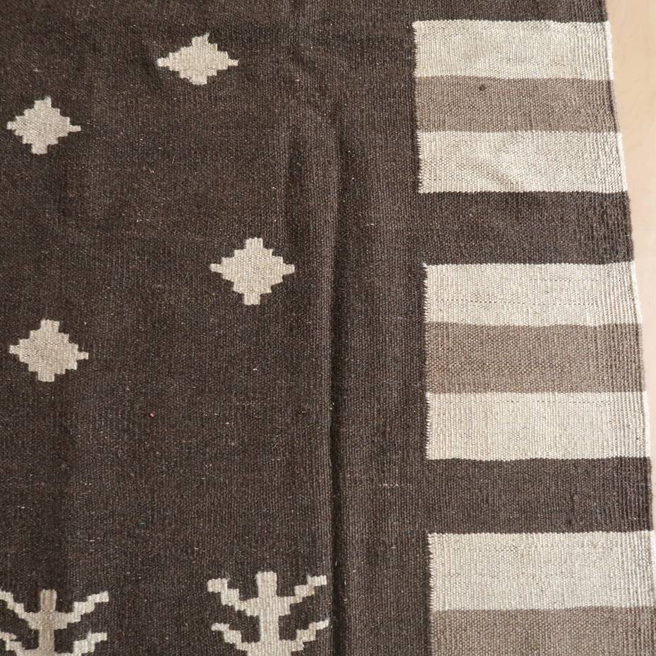 落ち着いたブラウンのウール素材で手織りされたギャッベのラグは、幾何学模様とストライプが絶妙に配置され、専門店通販のペルシャ絨毯として床に並んでいる。