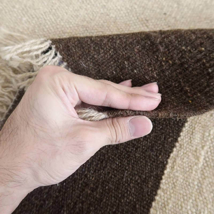 手織りのギャッベラグの厚みを指先で確認し、ウールの温かみと織り目の精緻さが際立っている。