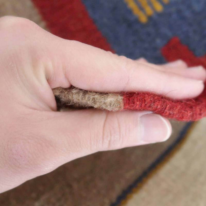 手で厚さを確認できる手織りのギャッベラグは、ウールのぬくもりと落ち着いた色合いが美しいペルシャ絨毯の一部が見える。