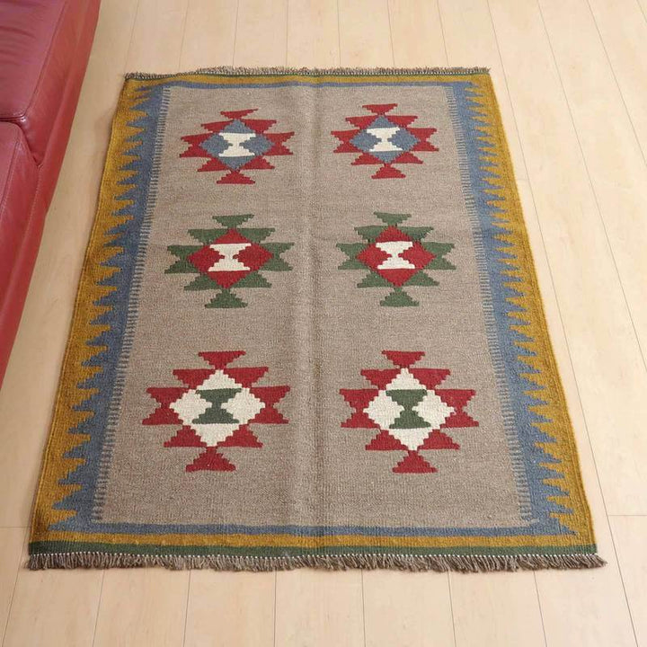 キリム・シラーズ／カシュガイ 141×102cm（KM-432）は、ブラウンを基調に赤や緑の幾何学模様が特徴的な手織りのギャッベラグがリビングの床に敷かれている。