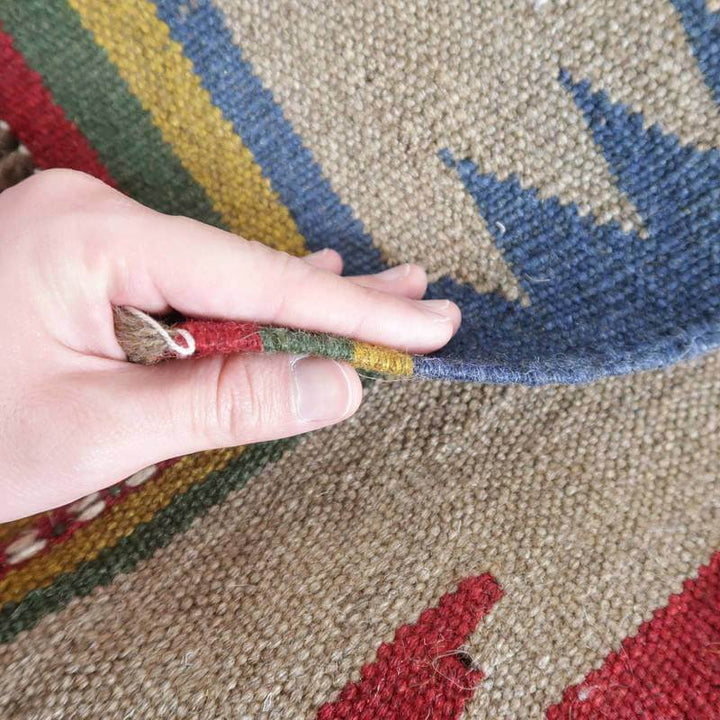 手織りのギャッベラグが指でめくられ、その厚みやウールの質感が繊細に映し出されている。