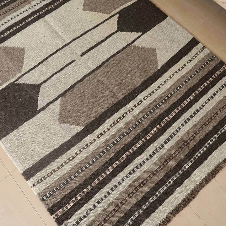 落ち着いた色合いのウール製ギャッベラグが、手織りの細やかな模様が際立つペルシャ絨毯専門店の通販商品として床に敷かれている。