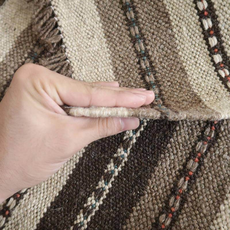 手織りのギャッベの厚みが指で示され、ウールの柔らかさとペルシャ絨毯の繊細な模様が際立っている。