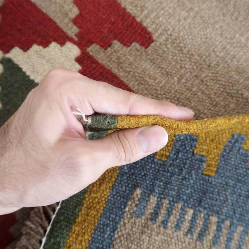 手に取られたギャッベラグの厚みや模様がはっきりと見える手織りのウール製品が、専門店の通販で購入可能です。