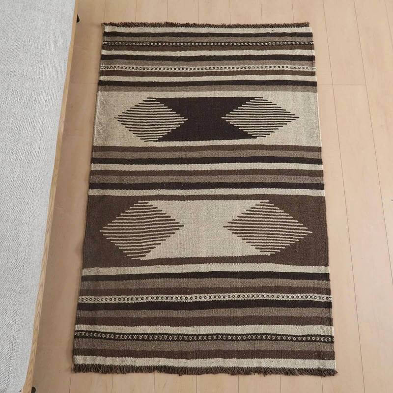 キリム・シラーズ／カシュガイ 150×99cm（KM-952）は、手織りのウール素材を用いたペルシャ絨毯専門店のギャッベラグが、落ち着いたブラウンとベージュの模様で床に並んでいる。