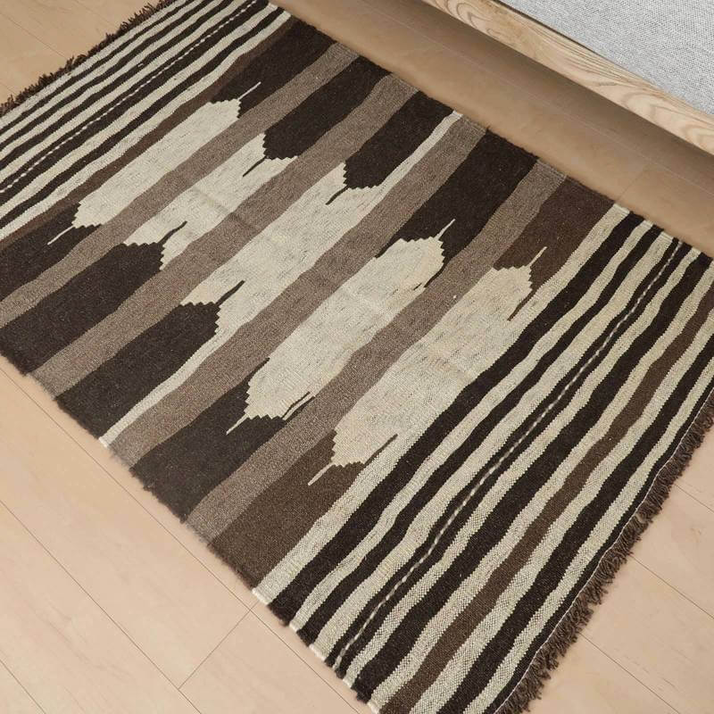 手織りのウール製ギャッベラグが床に広がり、ブラウンとベージュのストライプ模様が落ち着きを感じさせるリビングに映えている。