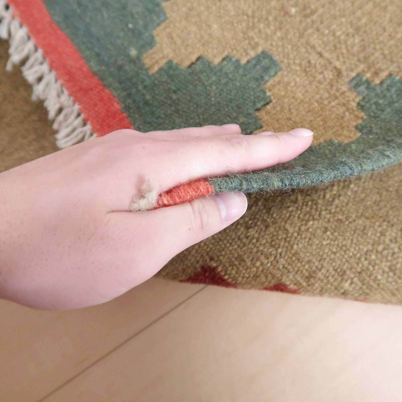 手で持ち上げられたギャッベのラグの端が見え、緻密な手織りの技術とウールの質感が際立っている。