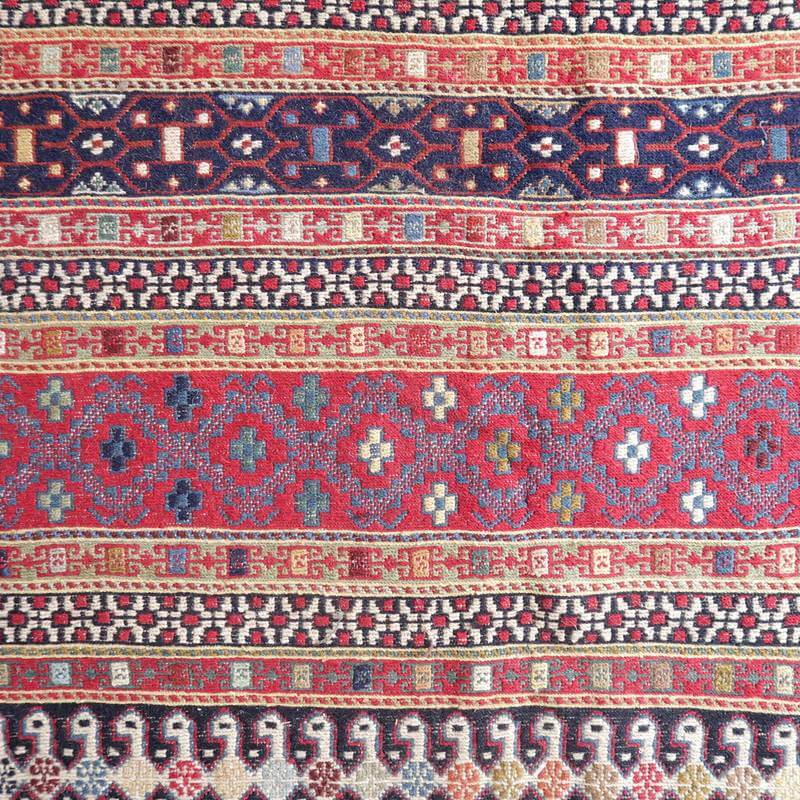 鮮やかな色彩と幾何学模様が美しい手織りのギャッベが広がり、ウール素材のぬくもりが感じられるペルシャ絨毯が床に敷かれている。