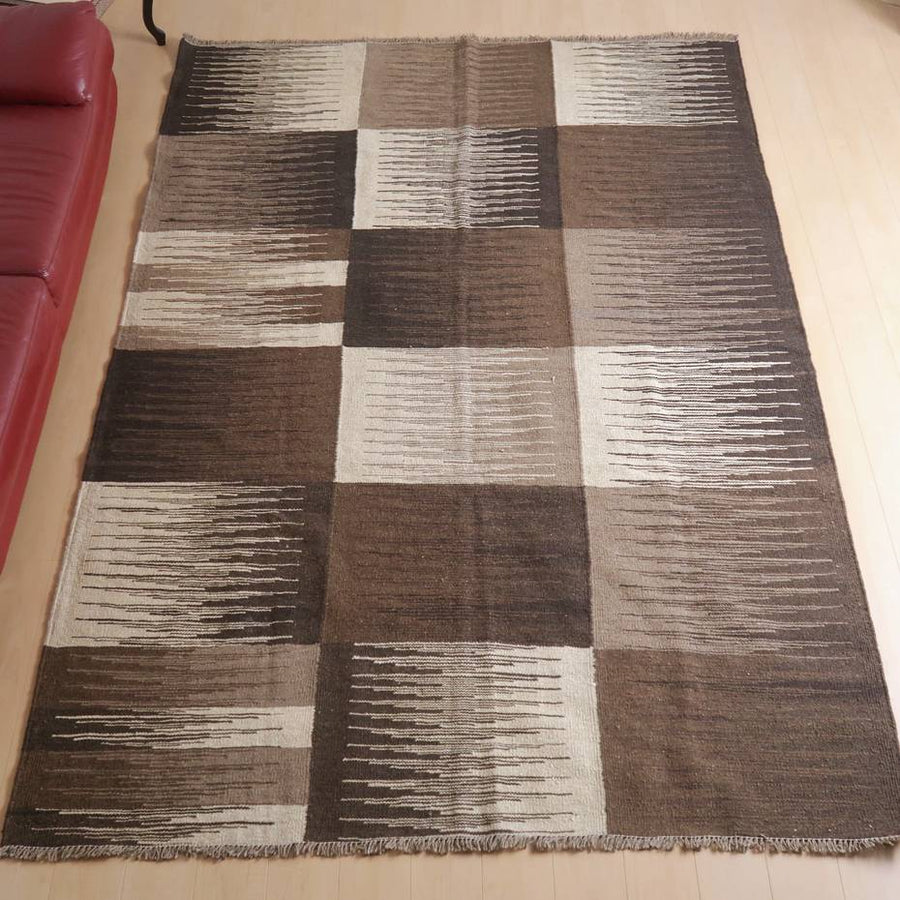 キリム・シラーズ／カシュガイ 300×202cm（KX-66385）は、ブラウンとベージュのパッチワーク模様が美しいウール製の手織りギャッベラグが、リビングルームの床に暖かさを添えている。