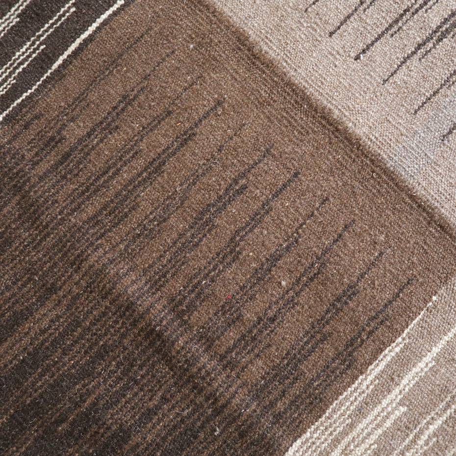 濃淡のあるブラウンの模様が丁寧に手織りされたウールのギャッベラグが床に広がり、落ち着きのあるペルシャ絨毯の質感が際立っている。