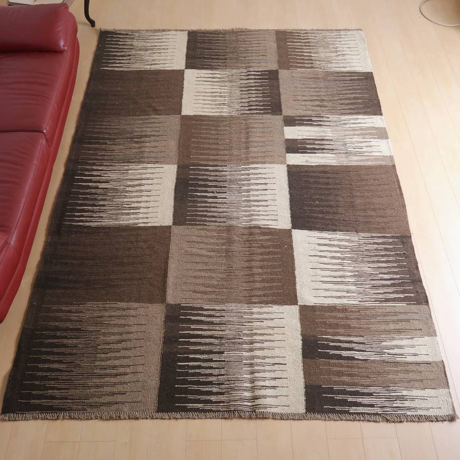 キリム・シラーズ／カシュガイ 297×202cm（KX-66386）は、幾何学模様のブラウンとベージュが織りなす手織りのギャッベラグが、温かみのあるリビングの床に敷かれている。