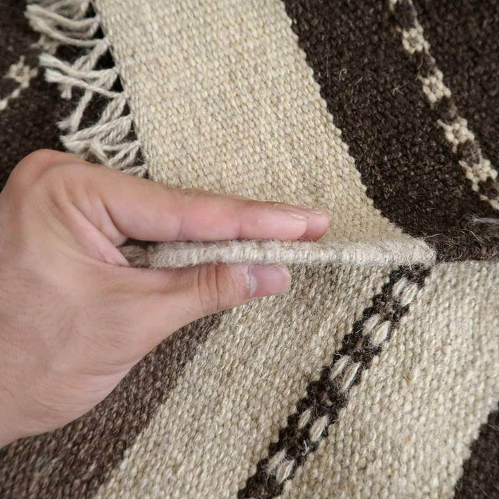 手織りのウール製ギャッベラグの厚みが指で示され、ぬくもりあるペルシャ絨毯の織り目が際立っている。