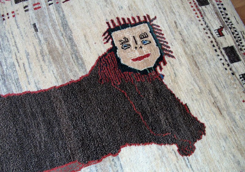 手織りのギャッベラグに描かれたユニークな顔の模様が、落ち着いたウール素材の中に個性を添えている。