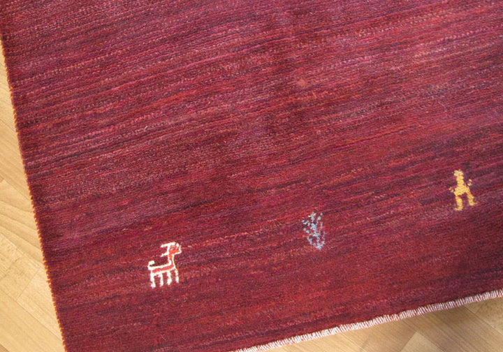 深みのある赤色の手織りウールのギャッベラグに、可愛らしい動物の模様が散りばめられ、床の木目と美しく調和している。
