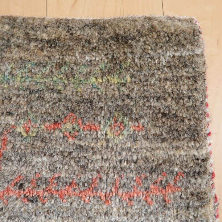 ブラウン系のギャッベが木製の床の上に敷かれており、赤や緑の模様が見える部分です。