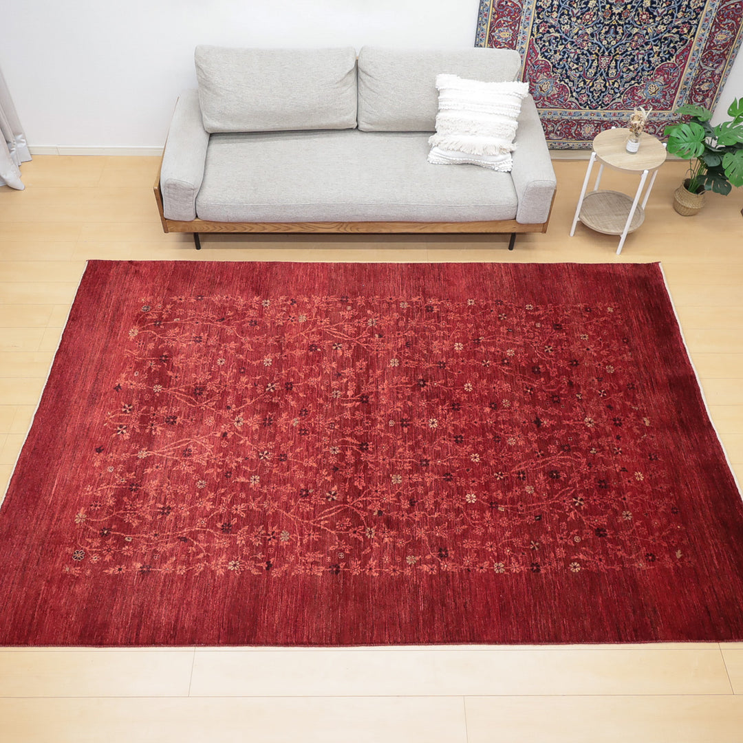 明るい木の床に置かれた赤い花柄のラグとグレーのソファ、白いクッションが見える部屋