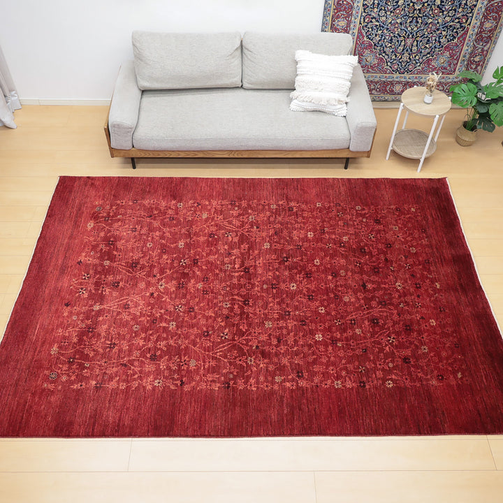 明るい木の床に置かれた赤い花柄のラグとグレーのソファ、白いクッションが見える部屋