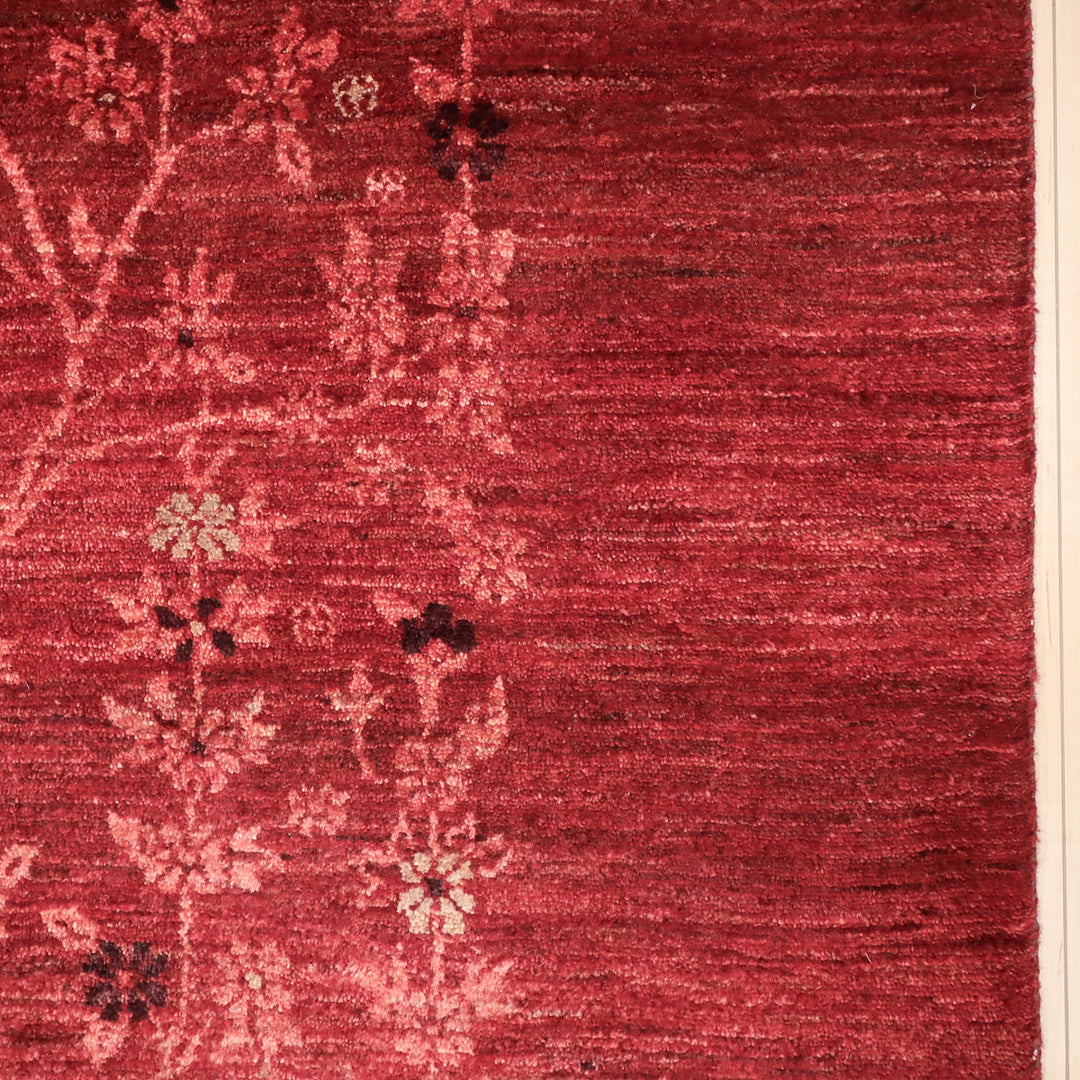 赤い地に淡いピンクやクリーム色の花柄が織り込まれたテクスチャのあるカーペットの一部