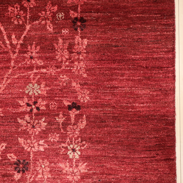 赤い地に淡いピンクやクリーム色の花柄が織り込まれたテクスチャのあるカーペットの一部