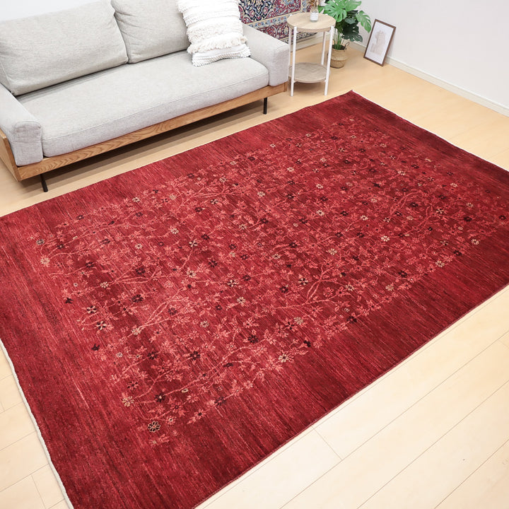 明るい木目の床に広げられた赤い花柄模様の大きなラグとグレーのソファがあるリビングルーム