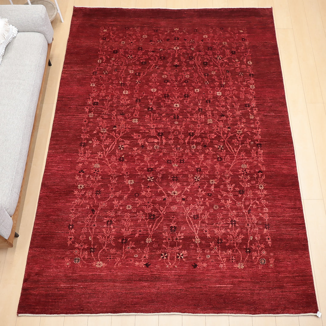 赤い地に繊細な花柄模様が広がるラグが明るい床に敷かれている様子。
